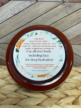 A jar of Tallow Skin + Face Lotion with a label that includes the ingredients and directions to use, placed on a woven mat with a wooden background.