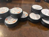 Multiple small jars with black lids, labeled as 'Tallow Skin + Face Lotion', and 'Magnesium Lotion' arranged on a wooden surface.