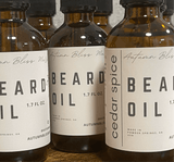 Bottles of beard oil with labels indicating 'Beard Spice' and 'Cedarwood'. Each bottle has a dropper and is labeled with the product name and the scent notes.