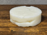 Round bar of tallow shampoo white soap on a wooden surface with a gray background
