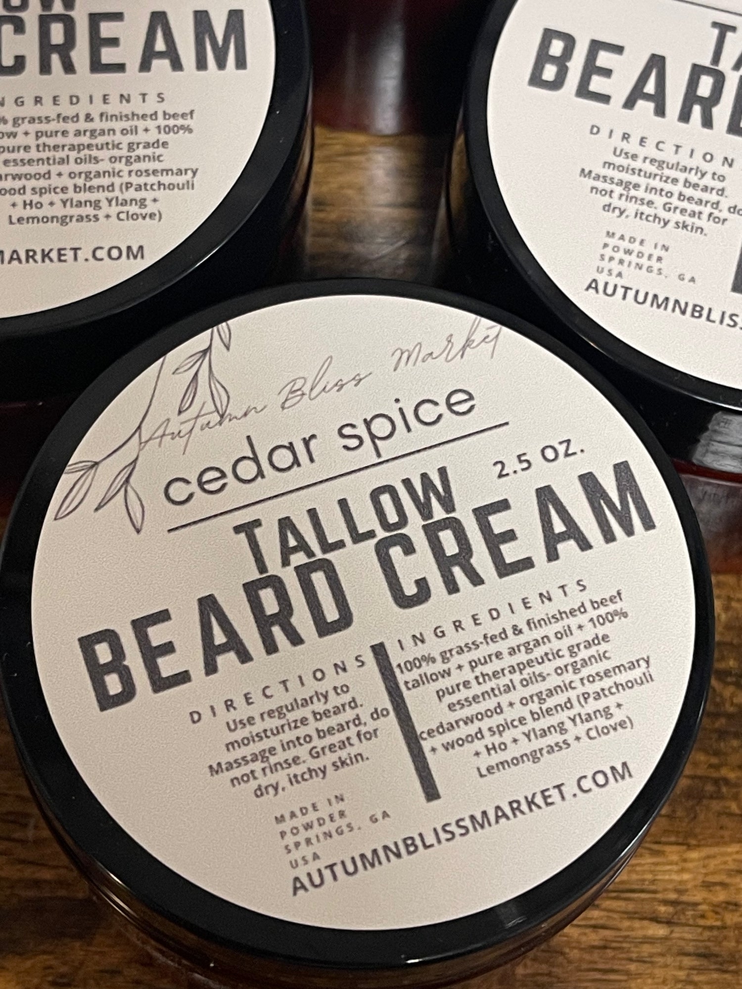 Jars of Tallow Beard Cream with labels indicating the product name and cedar spice scent on a wooden surface.