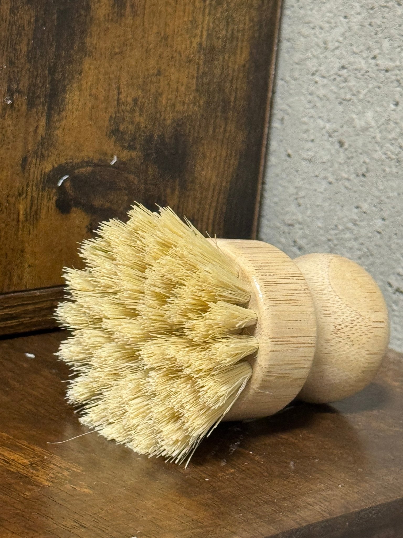 Bristle dish brush on a wooden surface with a concrete wall in the background
