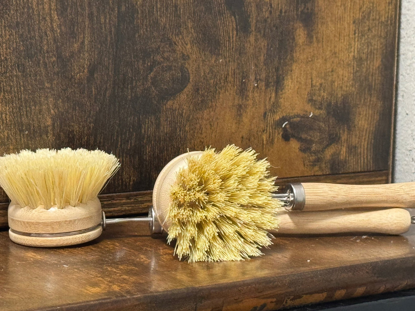Two long scrub brushes with natural bristles on a wooden surface.
