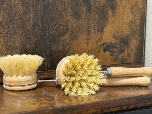 Two long scrub brushes with natural bristles on a wooden surface.