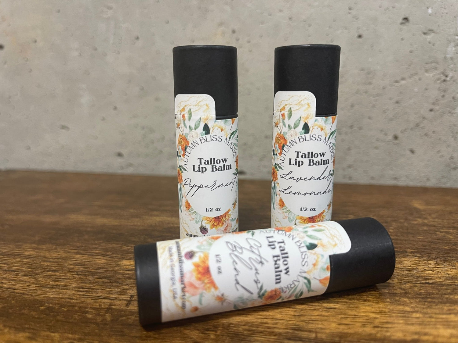 Three Tallow Lip Balm showing the different kinds of scents, placed on a wooden surface with silver background.