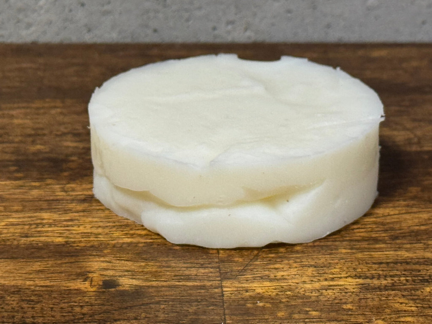 Round bar of tallow shampoo white soap on a wooden surface with a gray background